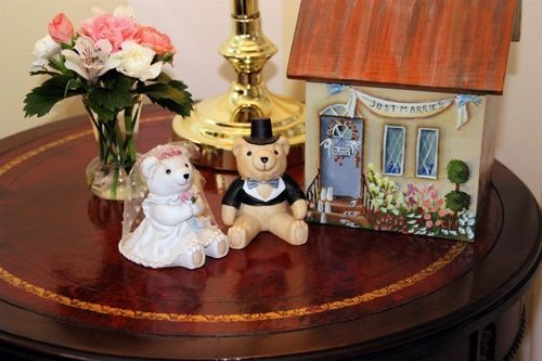 Two teddy bears are sitting on a table next to a small house