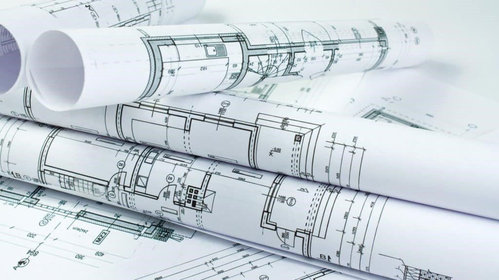 Several architectural blueprints are rolled and stacked on top of each other, displaying black technical floor plans.