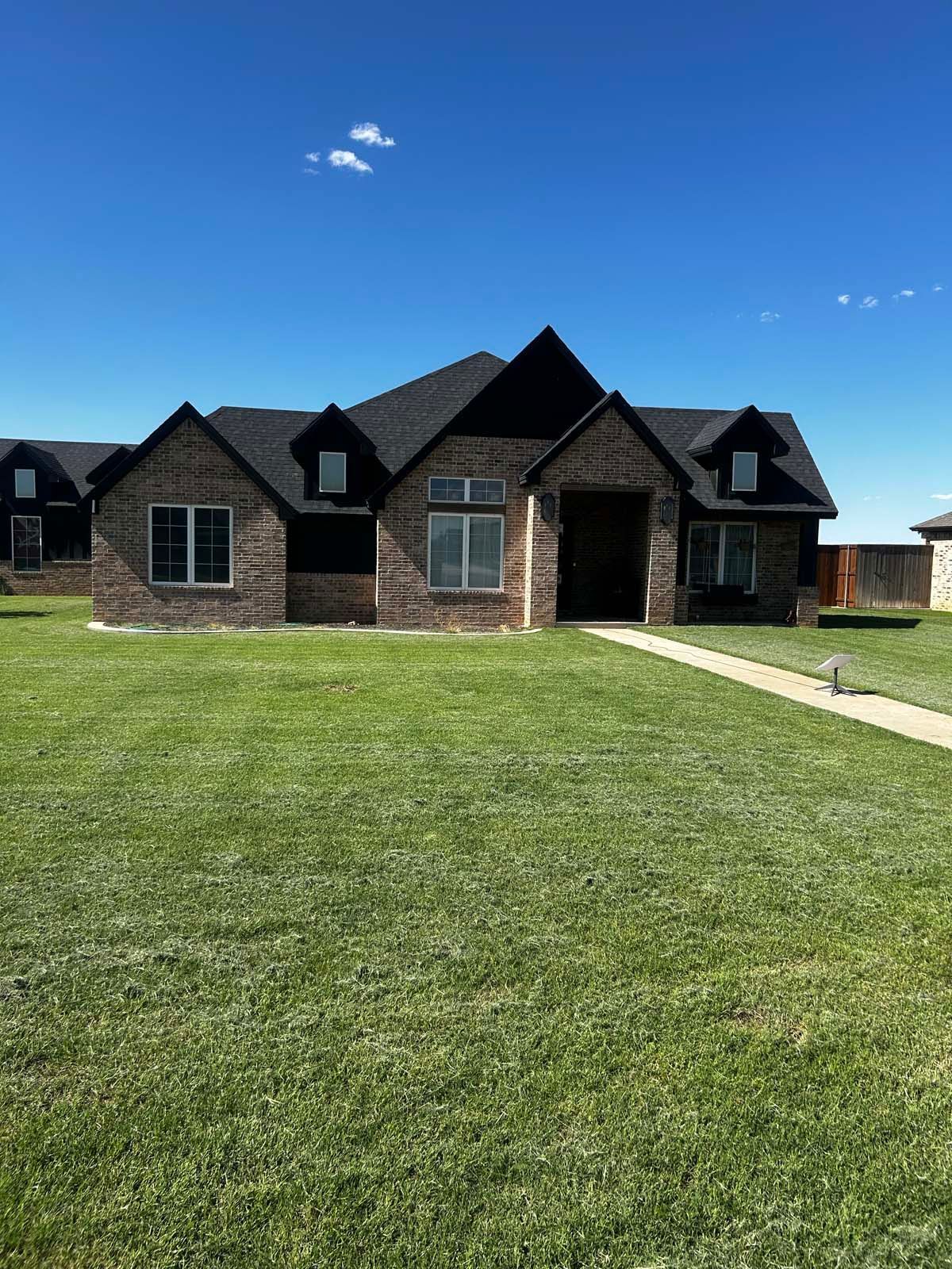 A large brick house with a black roof is sitting on top of a lush green lawn.