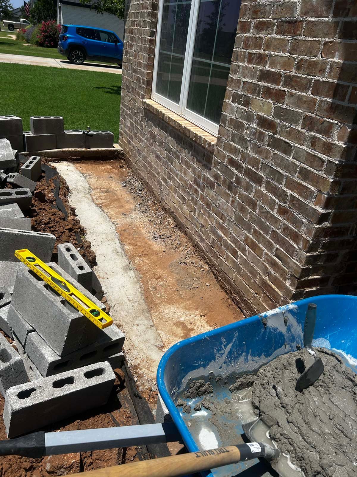 A wheelbarrow filled with cement is next to a brick wall.