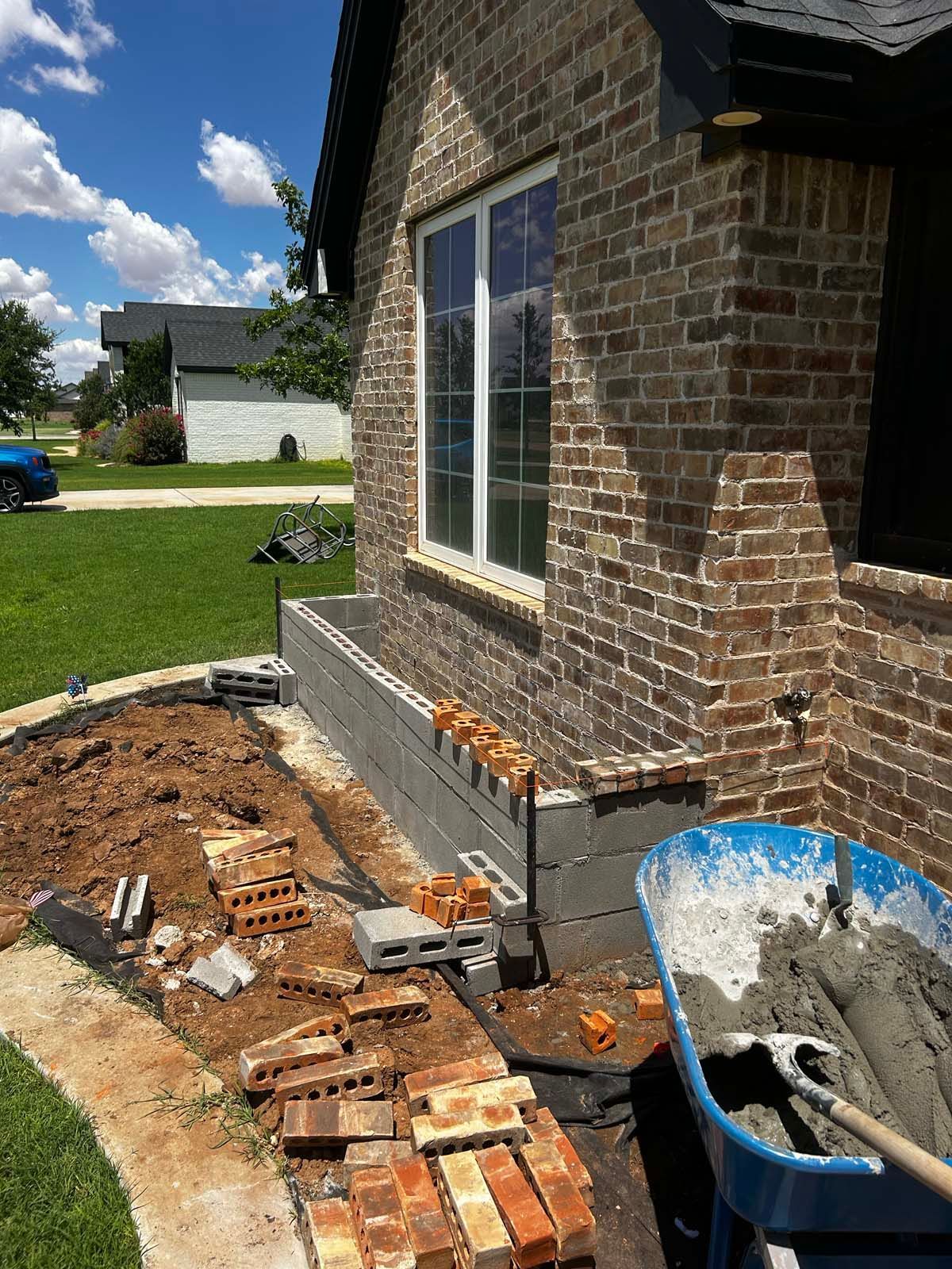 A wheelbarrow filled with cement is sitting in front of a brick building.