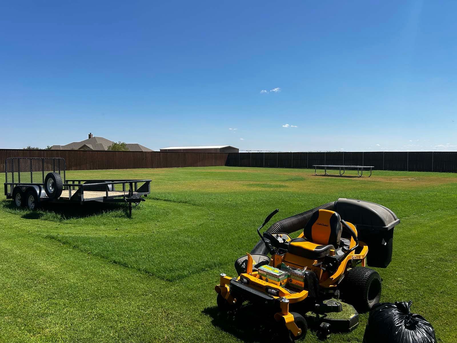 A yellow lawn mower is parked in a grassy field next to a trailer.