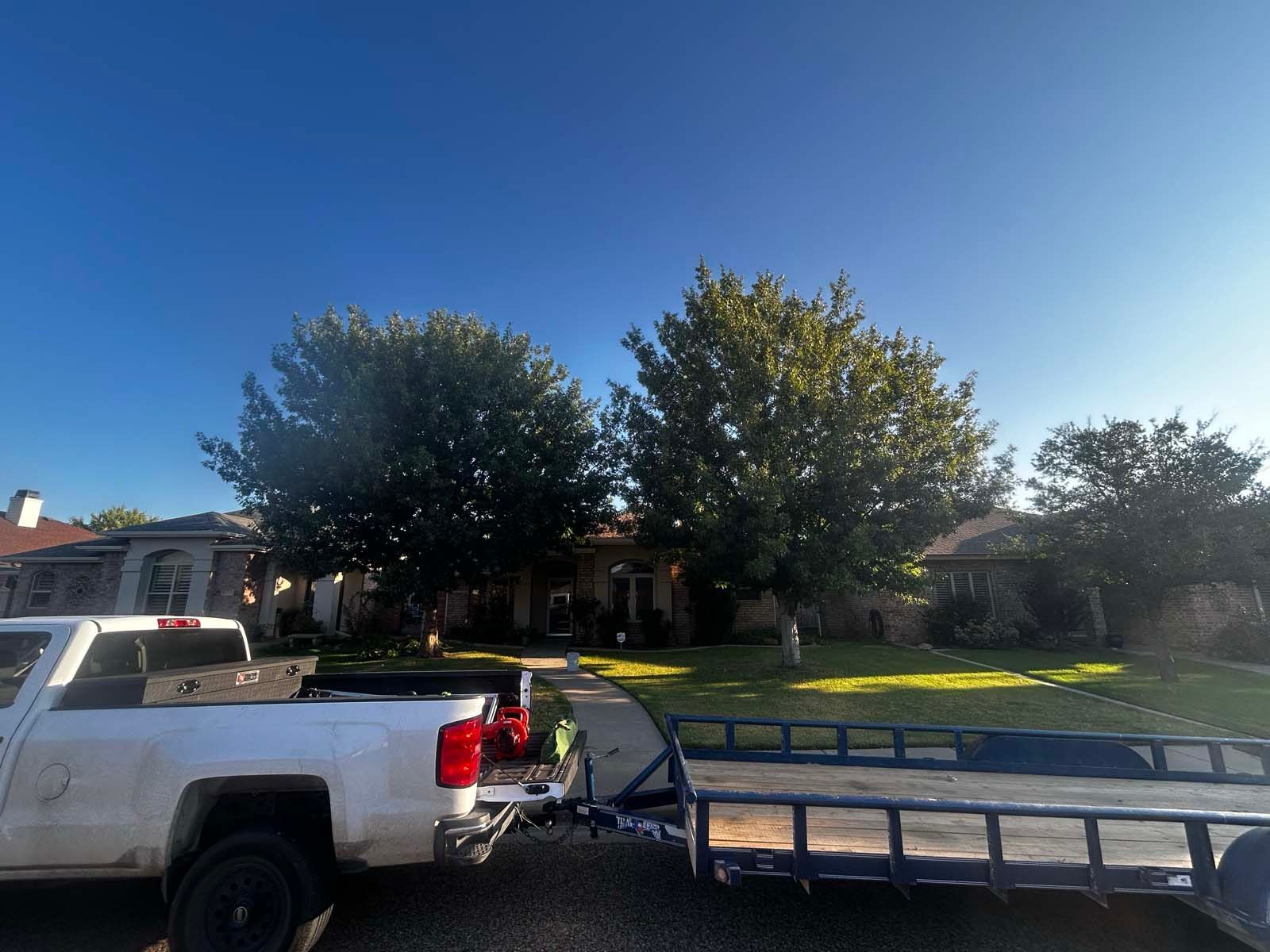 A white truck with a trailer attached to it is parked in front of a house.