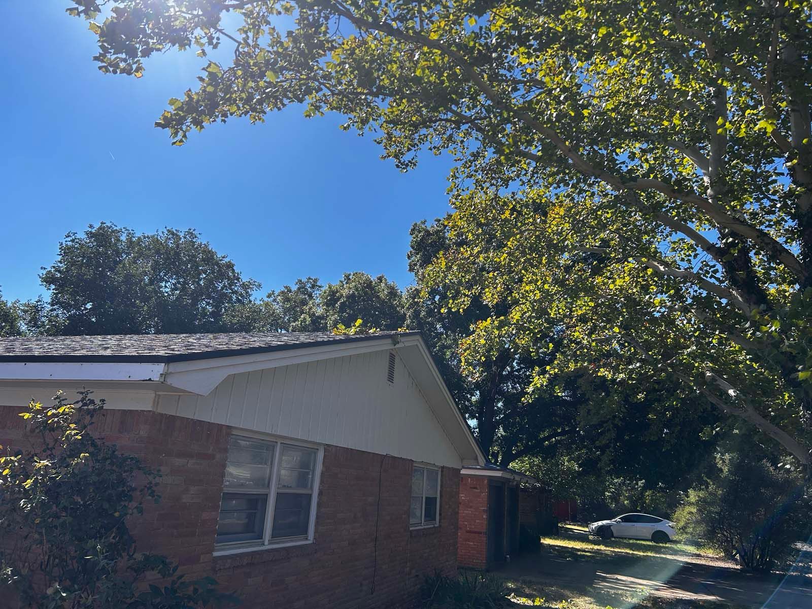 A brick house with a white roof is surrounded by trees on a sunny day.