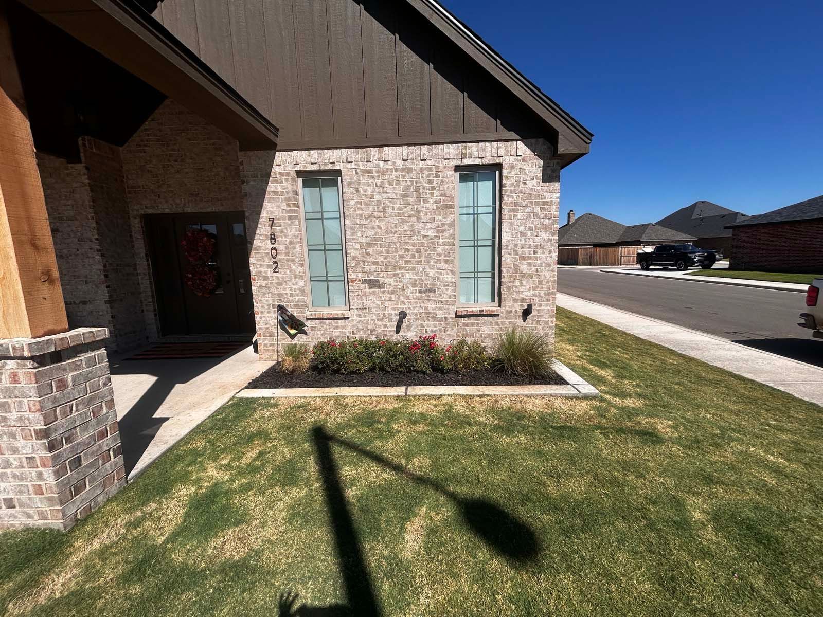 A brick house with a shadow on the grass in front of it.