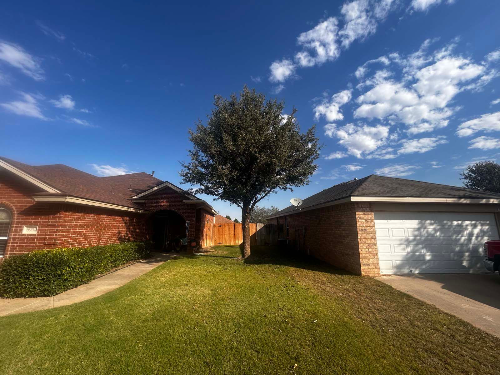 A brick house with a garage and a tree in front of it.