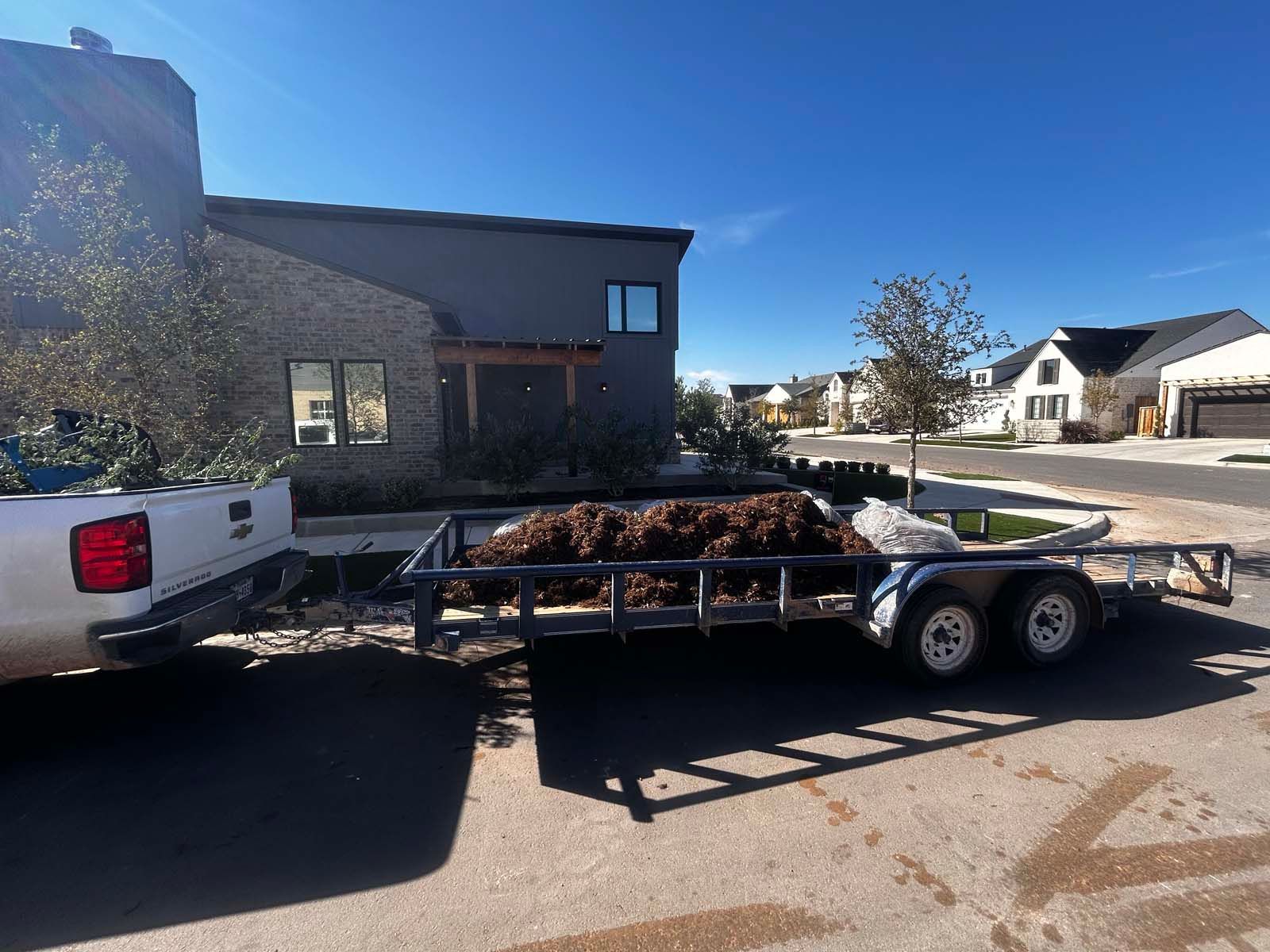 A white truck is pulling a trailer with a pile of dirt on it.