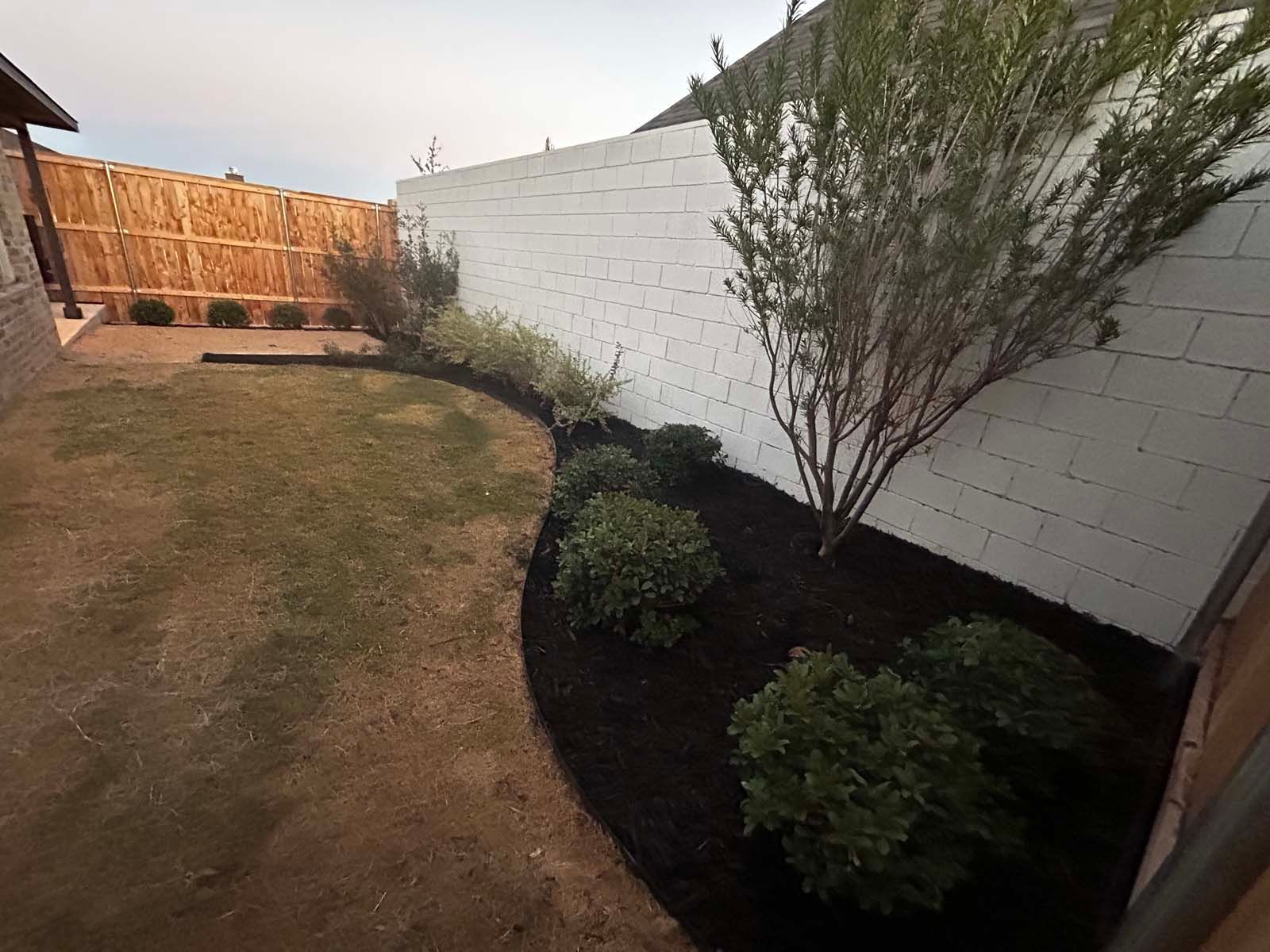 A backyard with a white brick wall and a fence surrounding it.