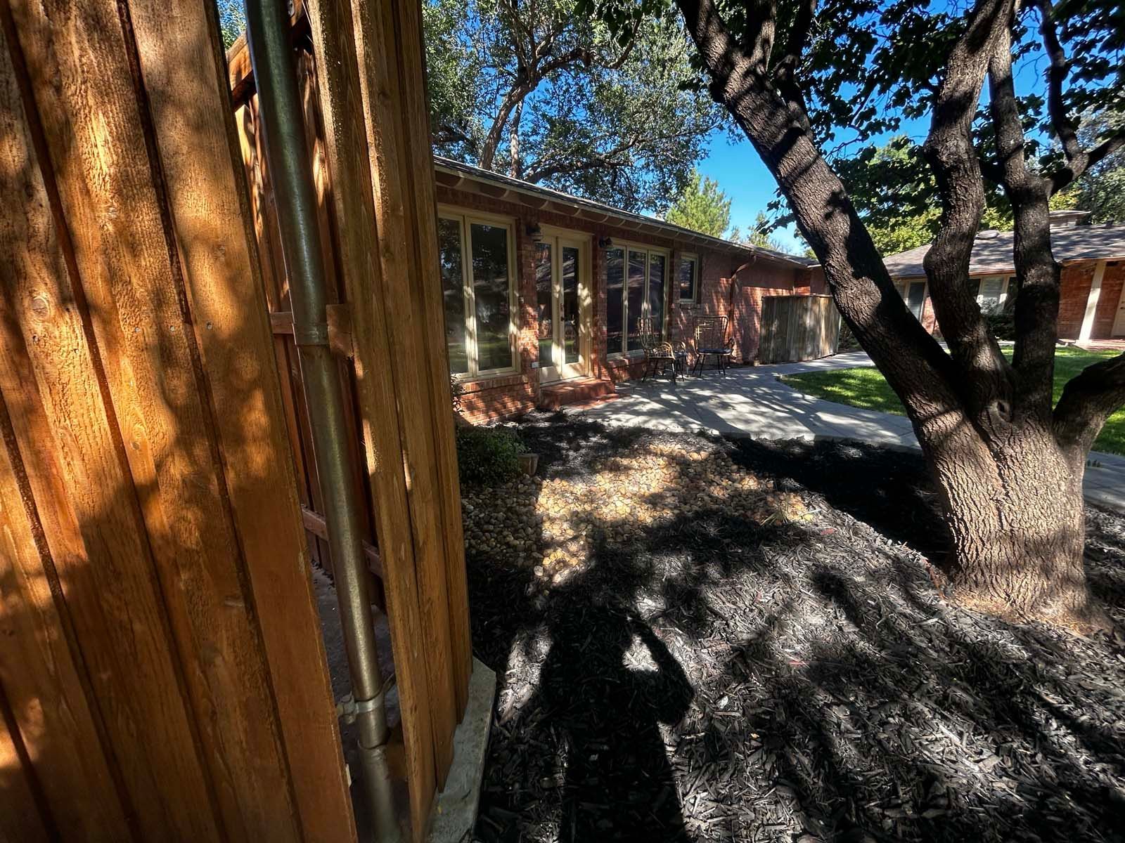 A house with a wooden fence and a tree in front of it.