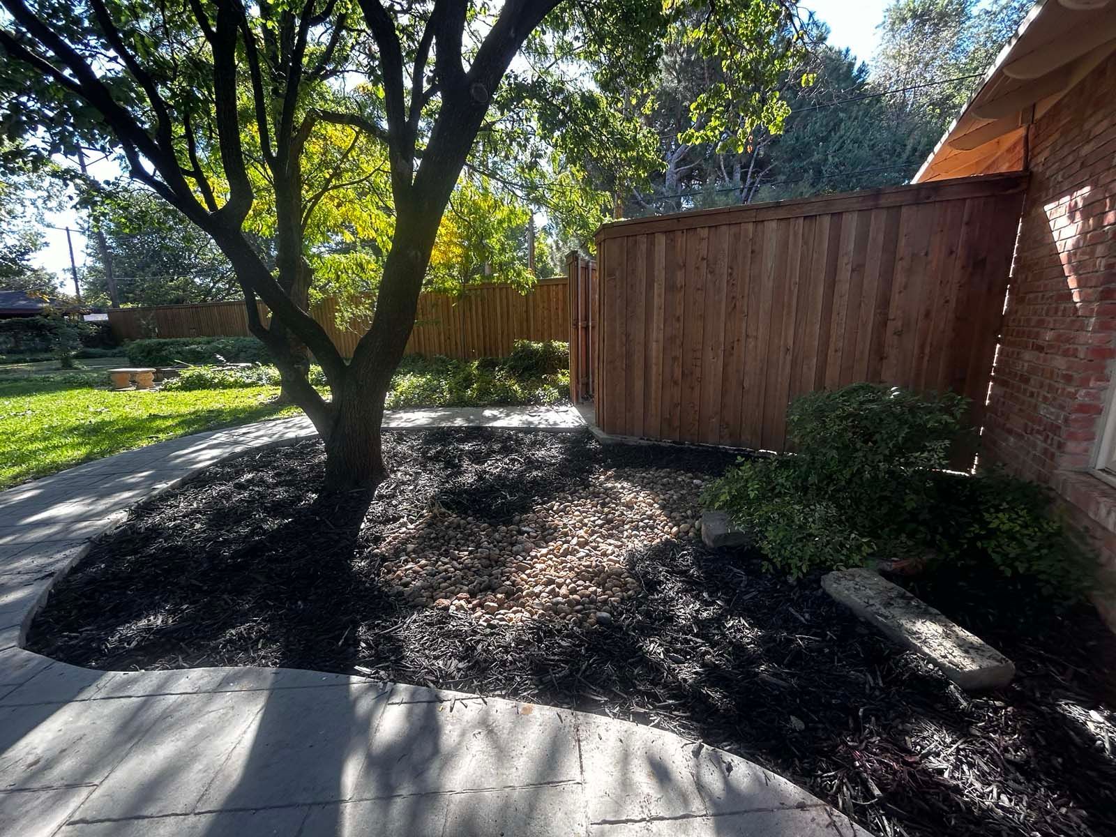 A brick house with a wooden fence and a tree in the backyard