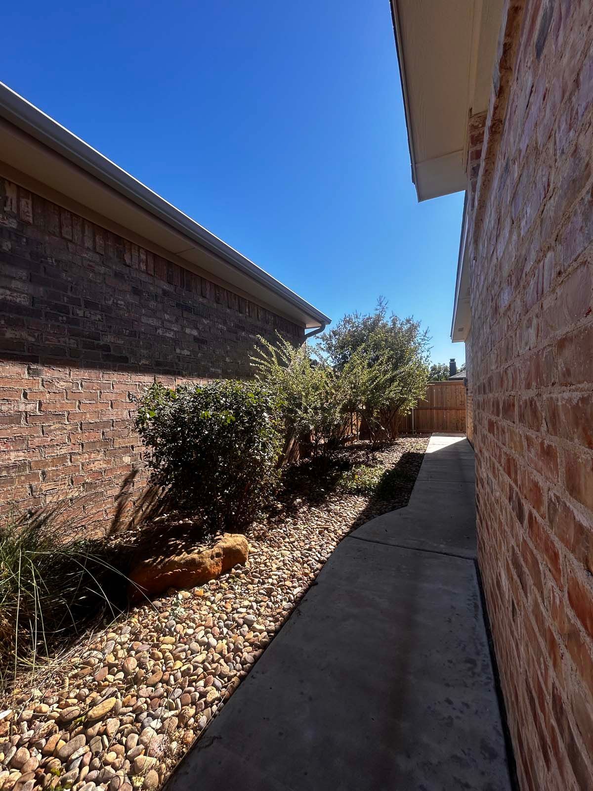 A sidewalk between two brick houses on a sunny day
