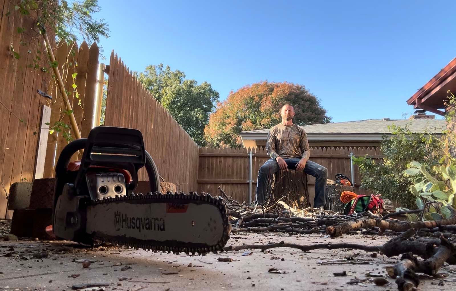 A man is sitting on a stump next to a chainsaw
