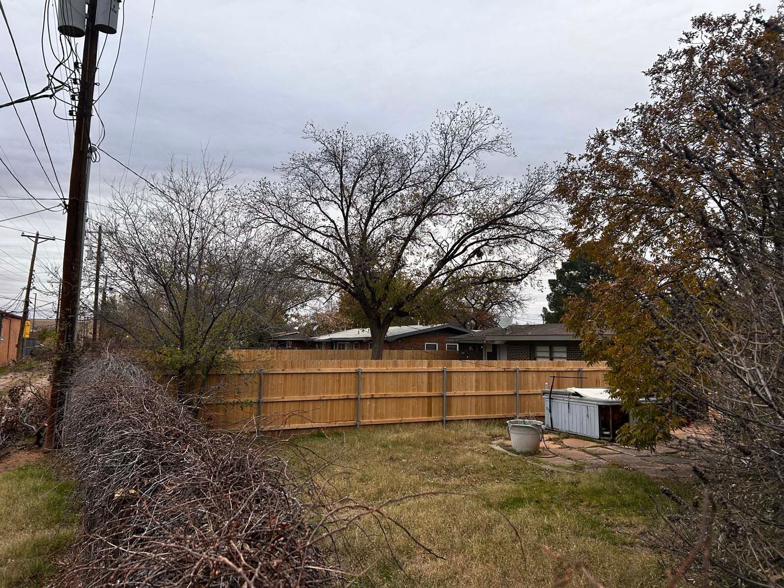 A wooden fence surrounds a yard with a house in the background.