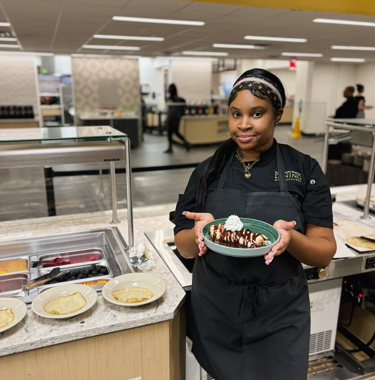 Chef holds a plate of crepes with toppings in a commercial kitchen setting.