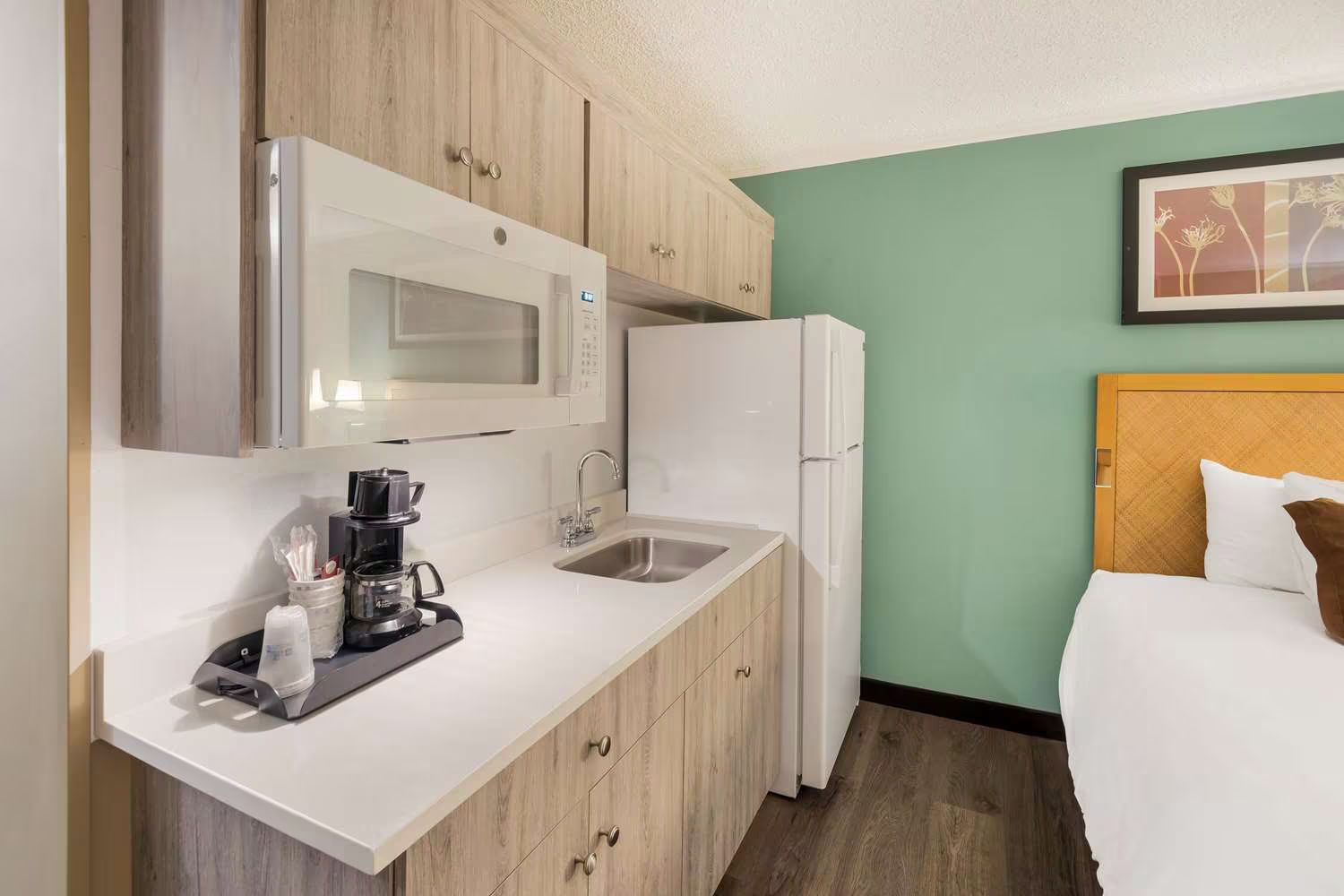 A hotel room with a kitchen , refrigerator , microwave , sink and coffee maker.