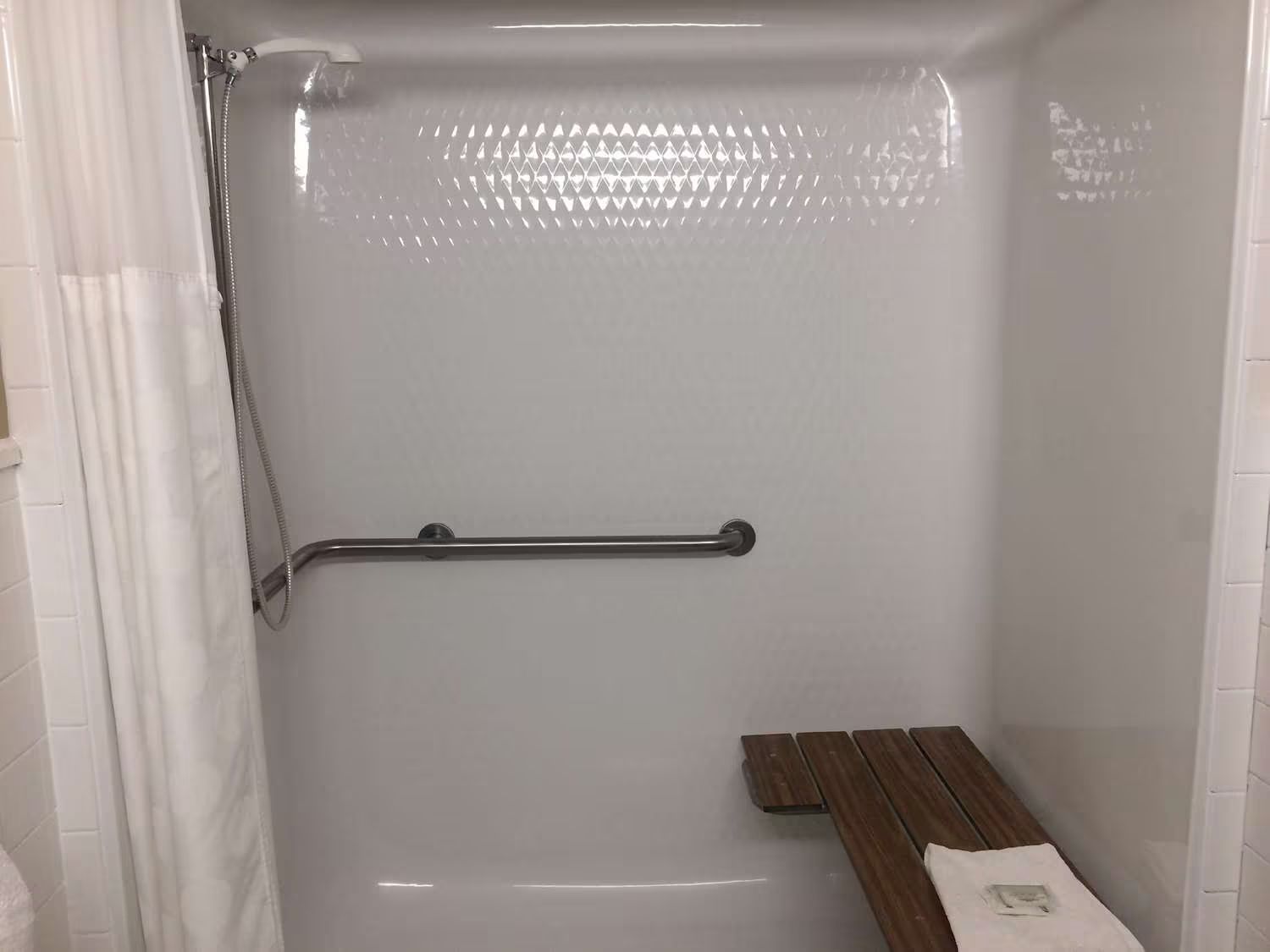 There is a wooden bench in the shower with a hand rail.