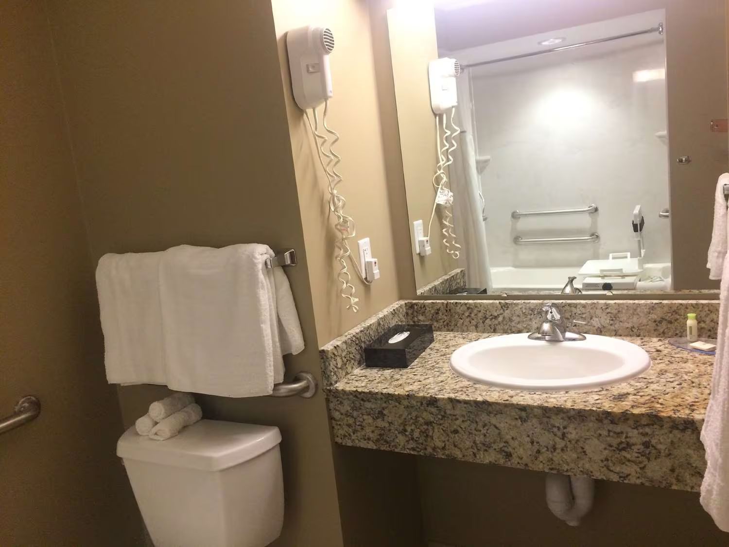 Bathroom with tan walls, granite countertop, white sink and toilet, and a mirror.
