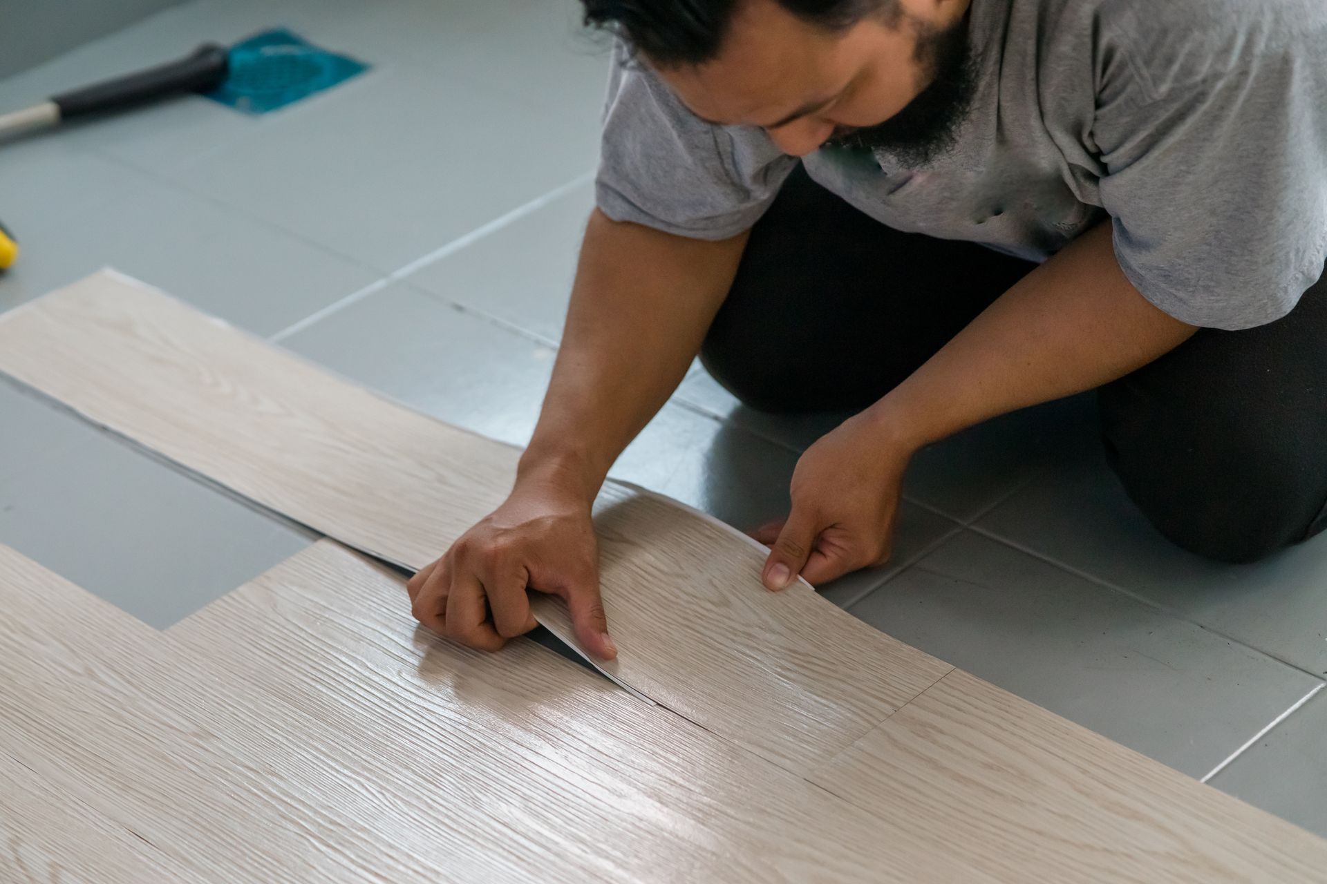 A man is kneeling on the floor cutting a piece of vinyl flooring.