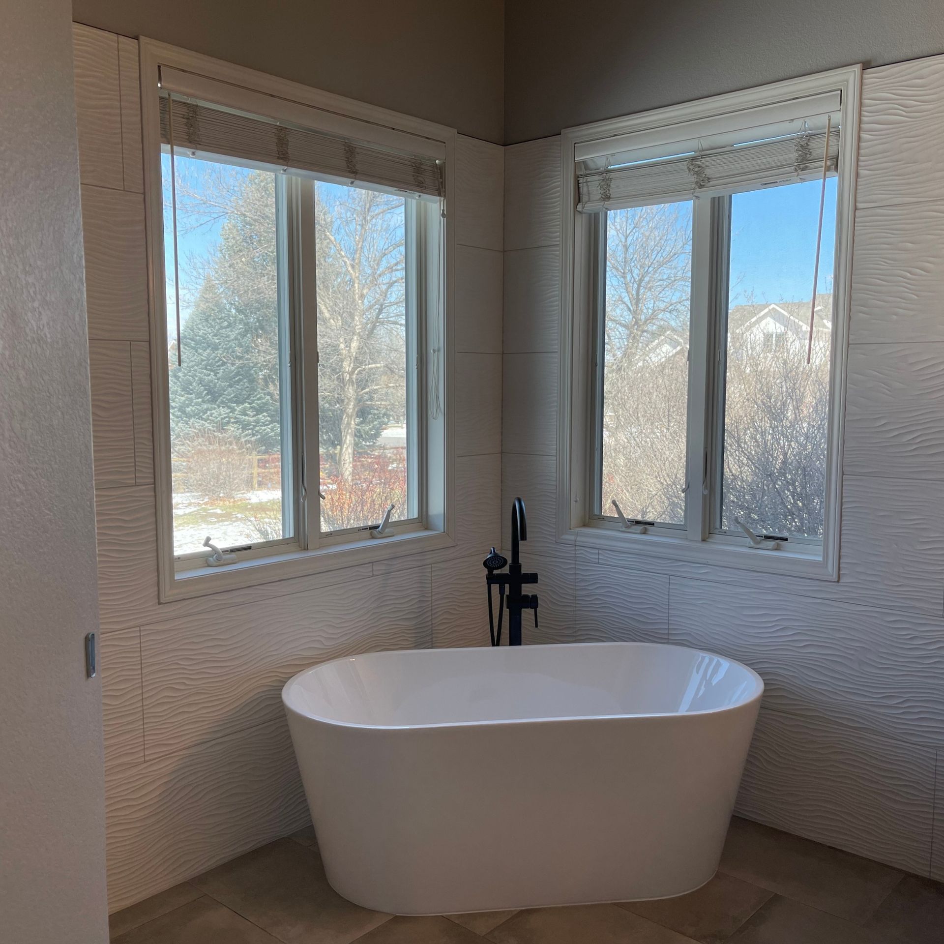 E.Squared Custom Plumbing Heating and Air - Bathroom with white tub, windows, and textured white tile walls. Black faucet.