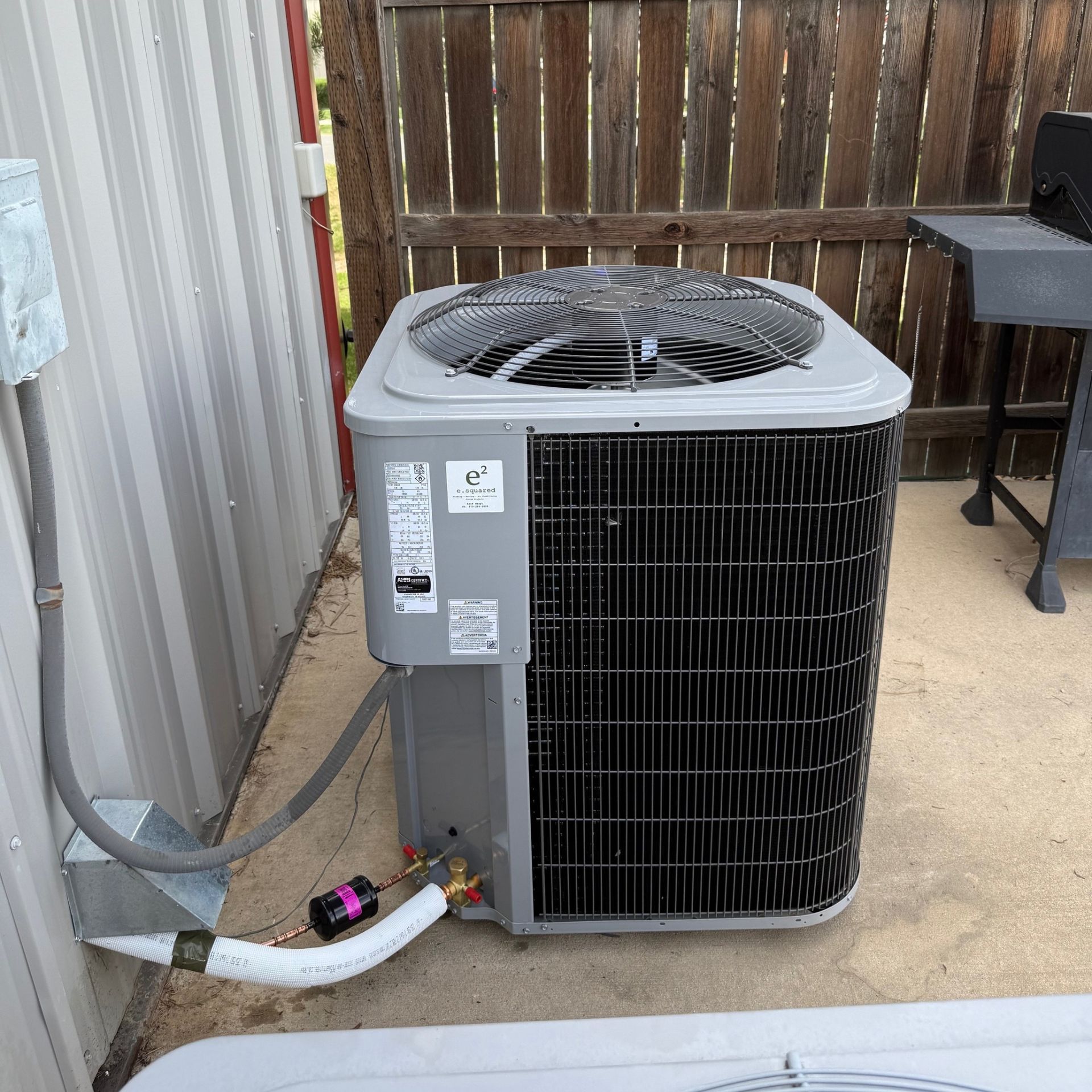 E.Squared Custom Plumbing Heating and Air - An air conditioning unit next to a building on a concrete surface.