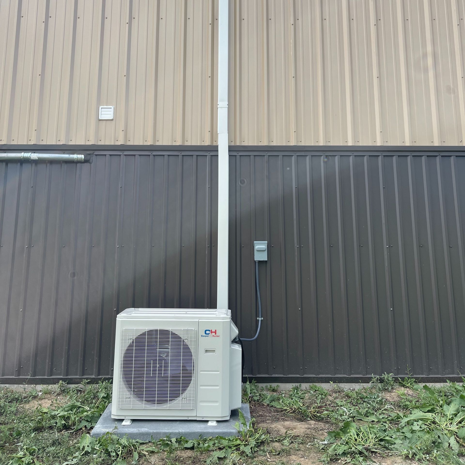 HVAC technician inspects AC unit on a rooftop, wearing safety gear and using a multimeter. Sunny day.