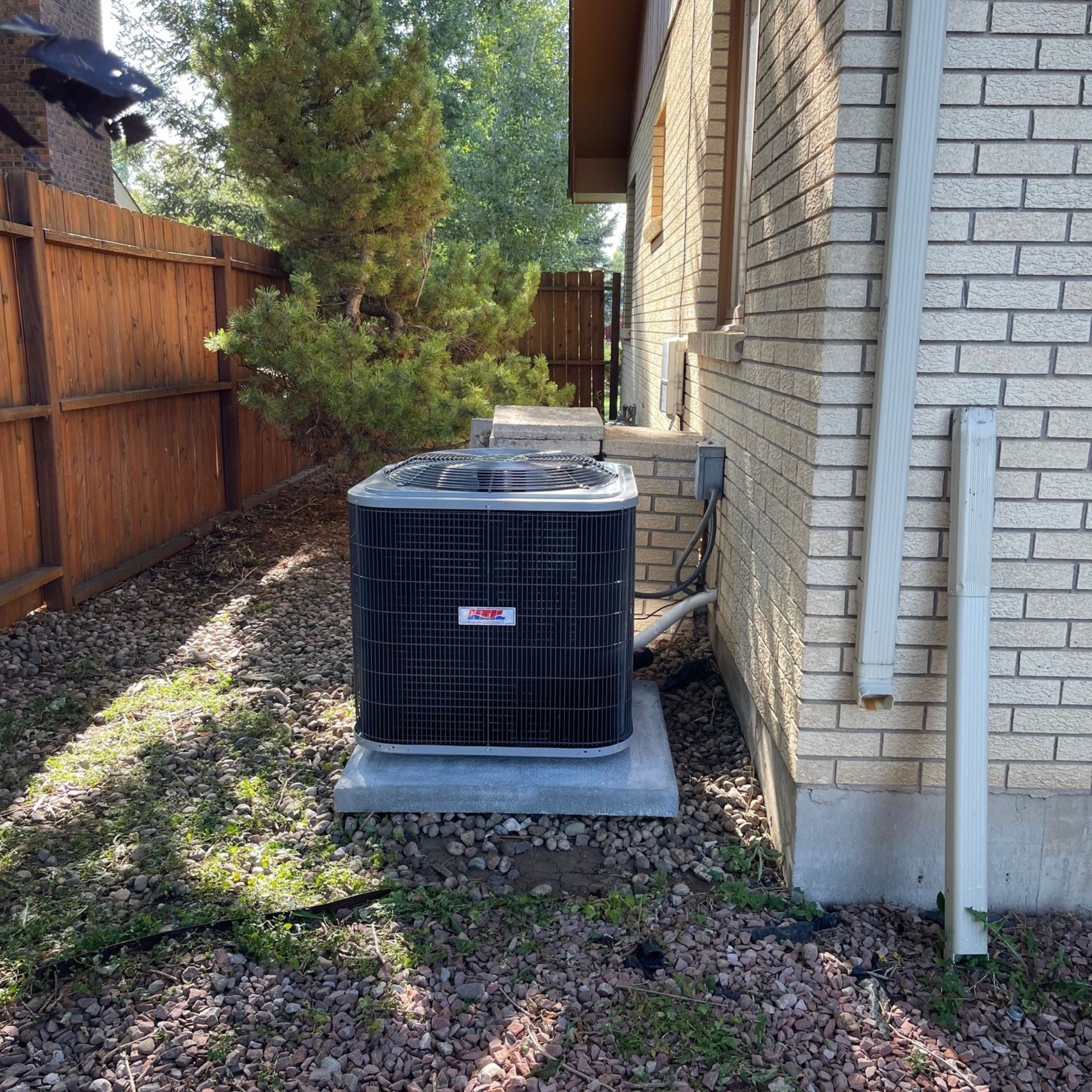 E.Squared Custom Plumbing Heating and Air - Air conditioner unit on concrete base next to brick house.