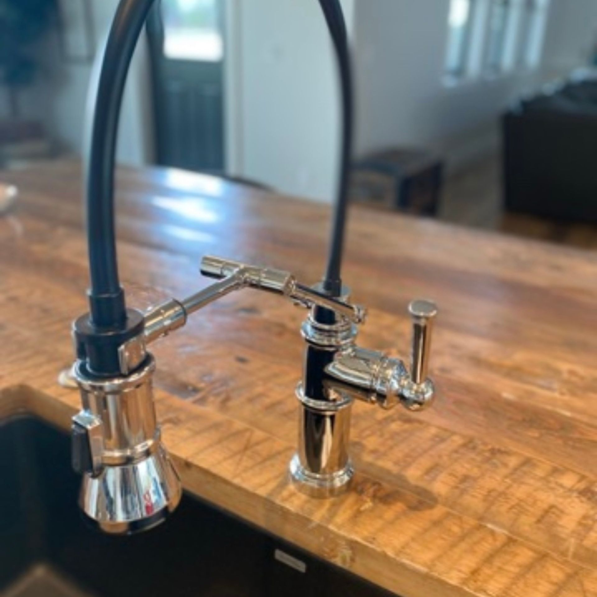 E.Squared Custom Plumbing Heating and Air - Shiny chrome kitchen faucet with black hose on a wooden countertop.