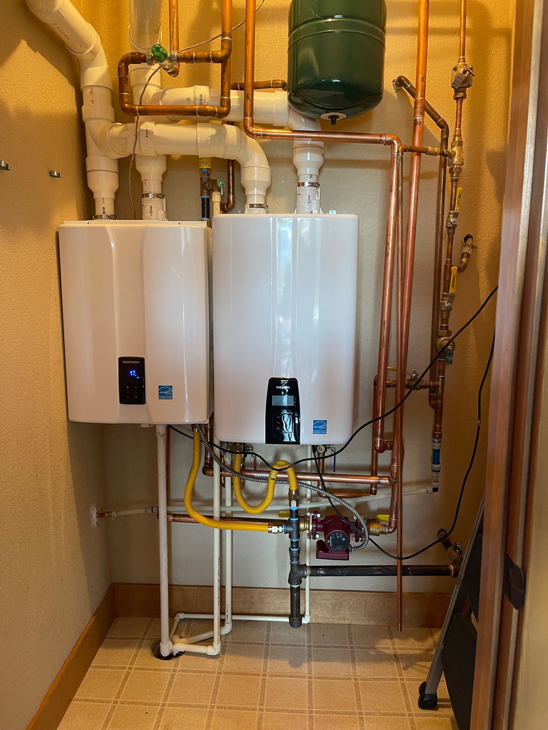 E.Squared Custom Plumbing Heating and Air - Two white tankless water heaters with copper pipes in a room.