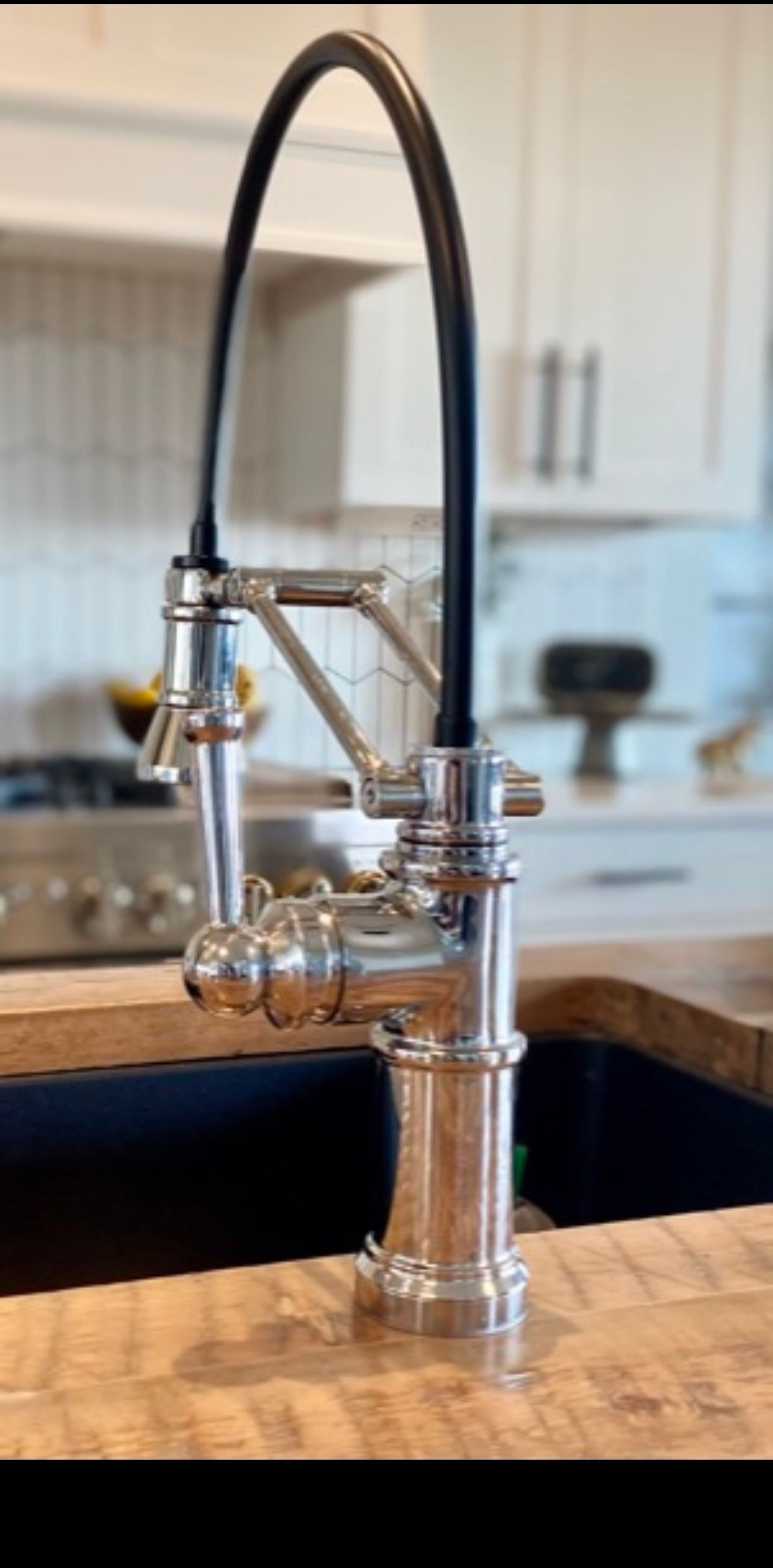 Silver kitchen faucet with a black hose against a light-colored kitchen backdrop.