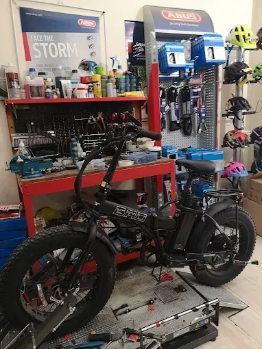 Bicicletta elettrica nera con pneumatici larghi in un'officina, con attrezzi e pezzi visibili.