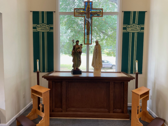 Altar with statue of Mary, Joseph and Jesus, crucifix, banners, and kneeling benches.