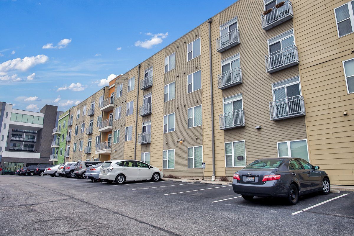 A parking lot in front of a large apartment building with cars parked in front of it.