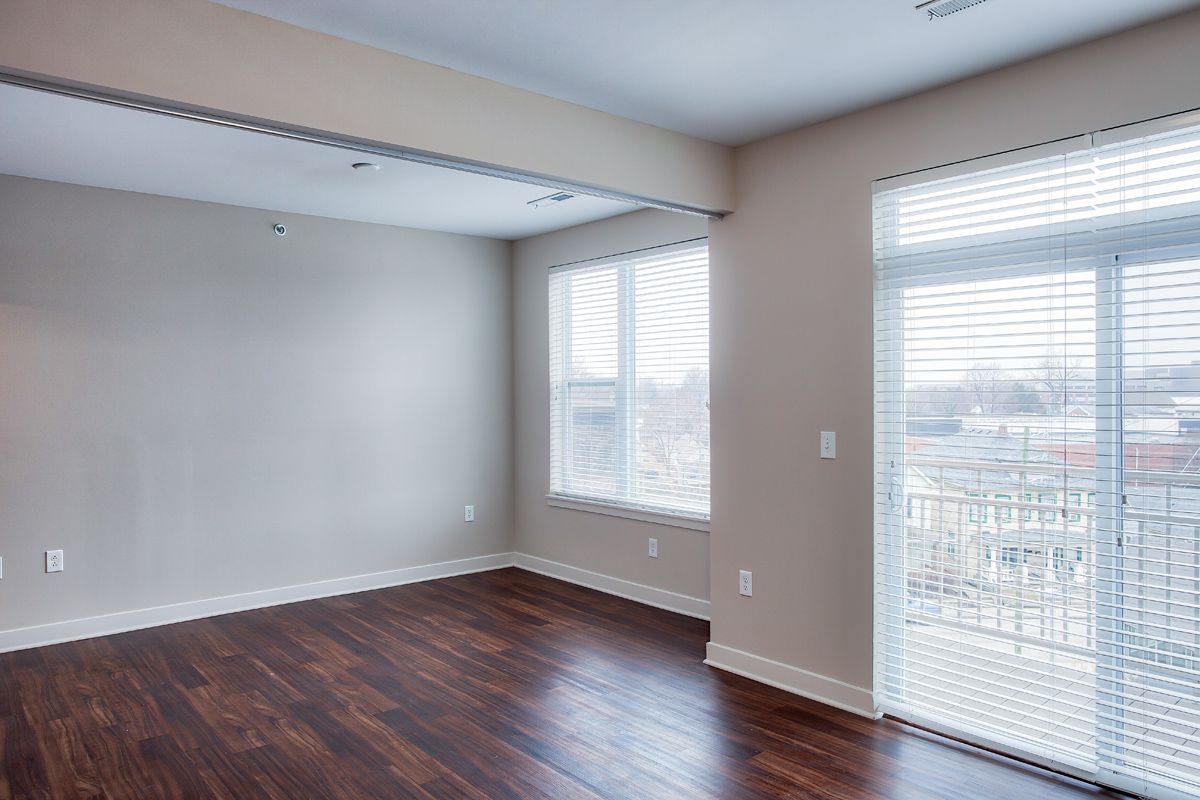 An empty living room with hardwood floors and sliding glass doors leading to a balcony.