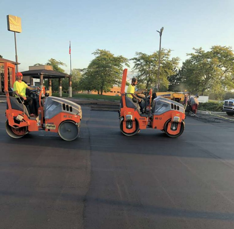 Two asphalt rollers are being used in a parking lot