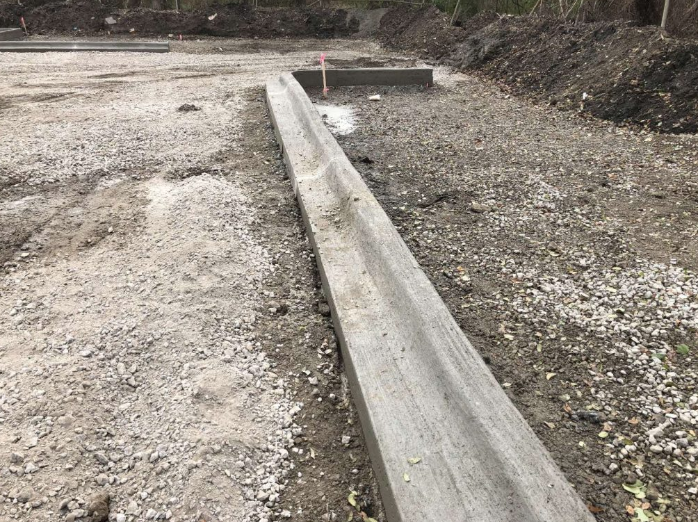 A concrete curb is being installed on a dirt road.