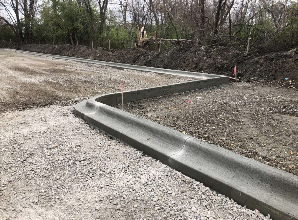 A concrete curb is being installed on a gravel road.