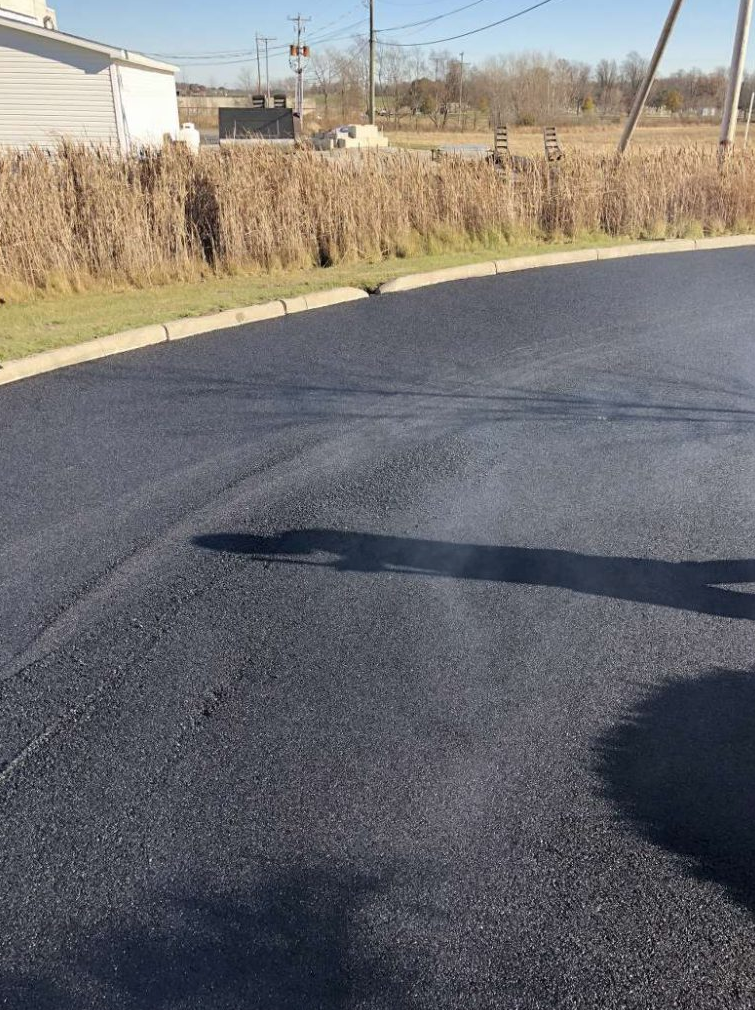 A shadow of a person is cast on a black asphalt road.