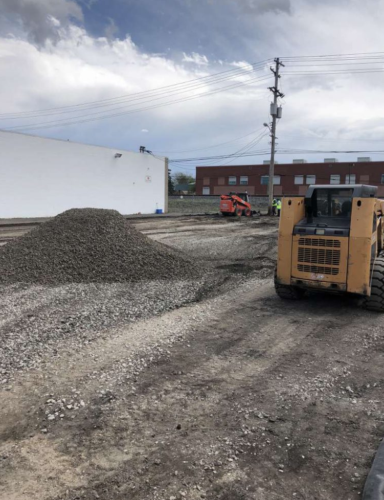 A bulldozer is driving down a dirt road next to a pile of gravel.
