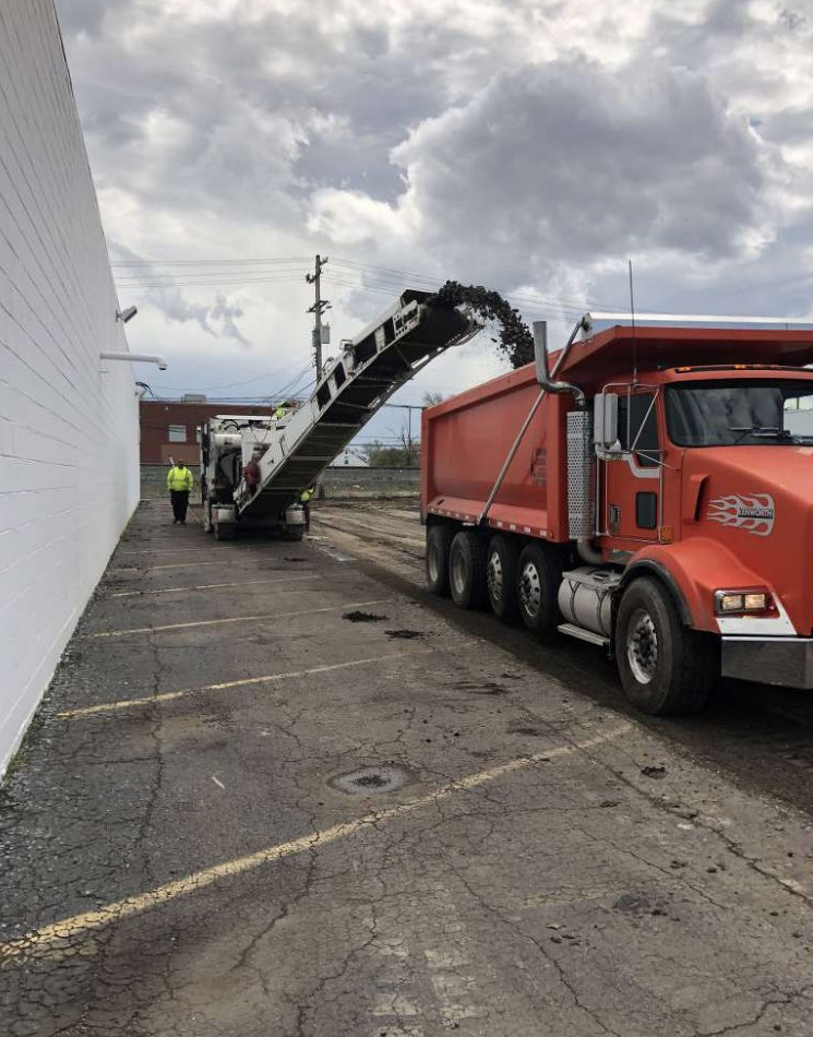 A red dump truck is parked in a parking lot next to a white building.