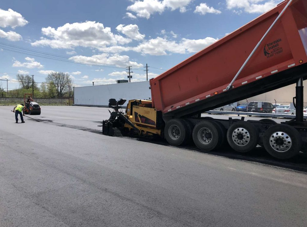 A dump truck is being loaded with asphalt in a parking lot.