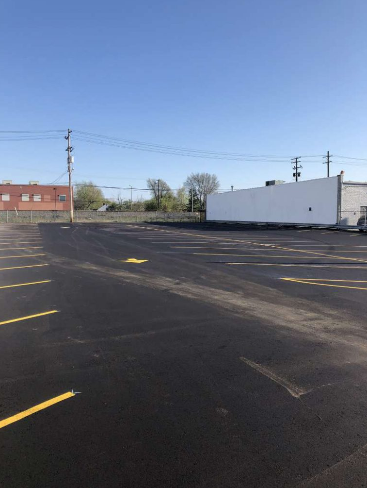 A parking lot with yellow lines and a white building in the background.