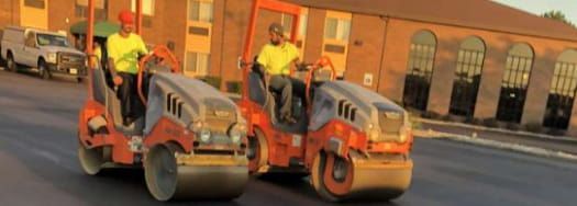 Two rollers are driving down a street in front of a building.