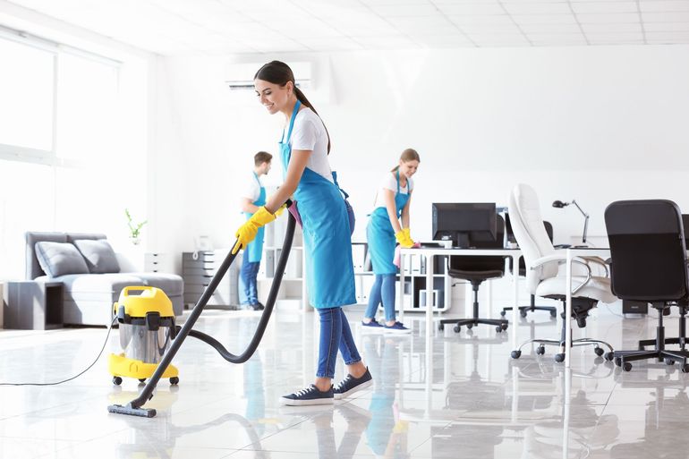 Cleaning staff vacuuming a bright modern office with desks and chairs. Cleaning staff vacuuming a bright modern office with desks and chairs.