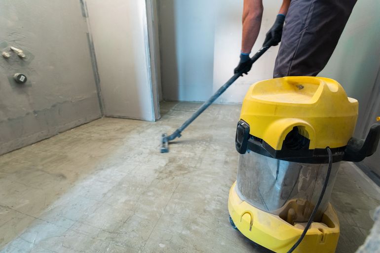 Person vacuuming a dusty concrete floor with a yellow wet-dry vacuum in an unfinished room. Person vacuuming a dusty concrete floor with a yellow wet-dry vacuum in an unfinished room.