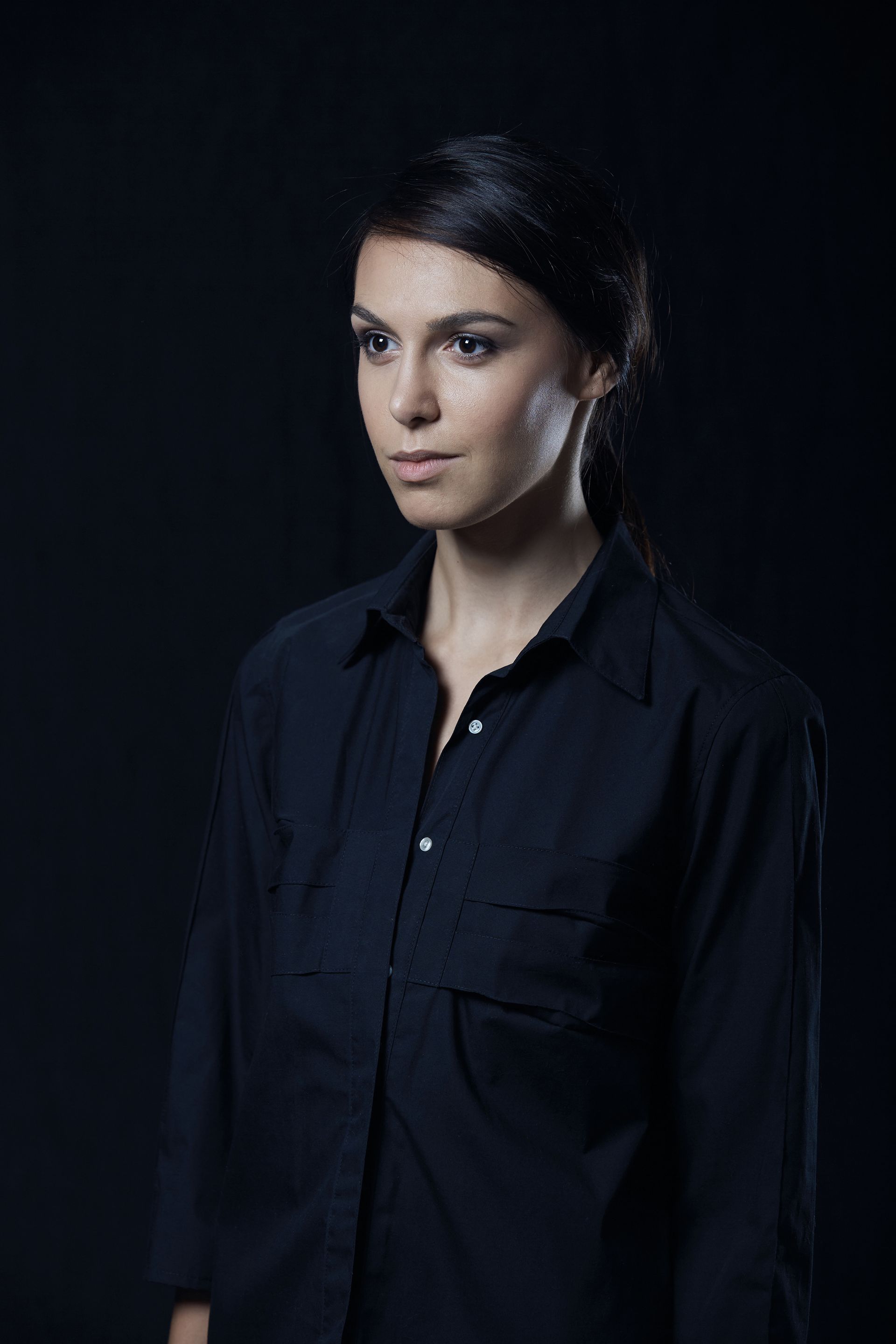 A woman in a black shirt is standing in front of a black background.