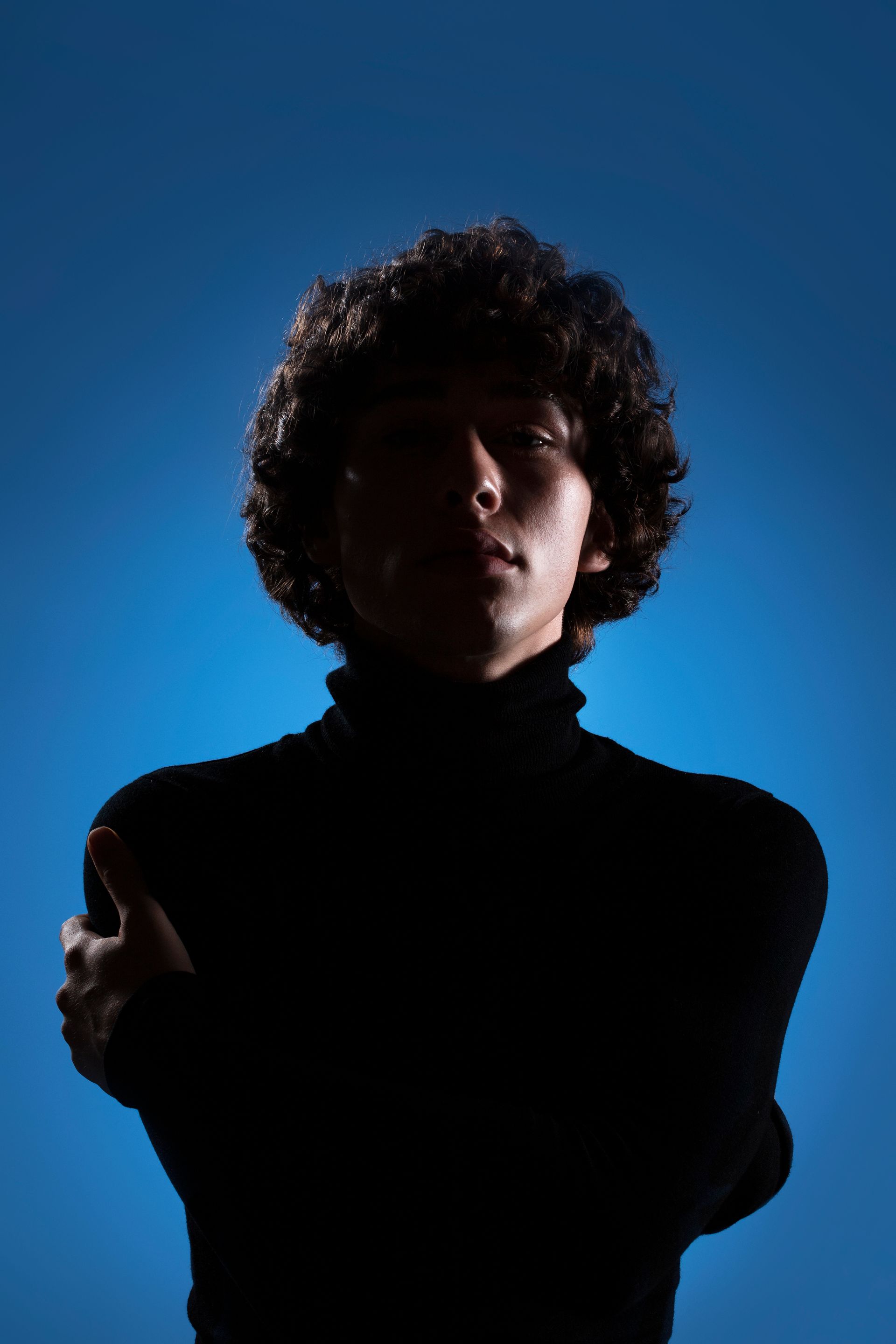 A silhouette of a man with curly hair wearing a black turtleneck sweater against a blue background.