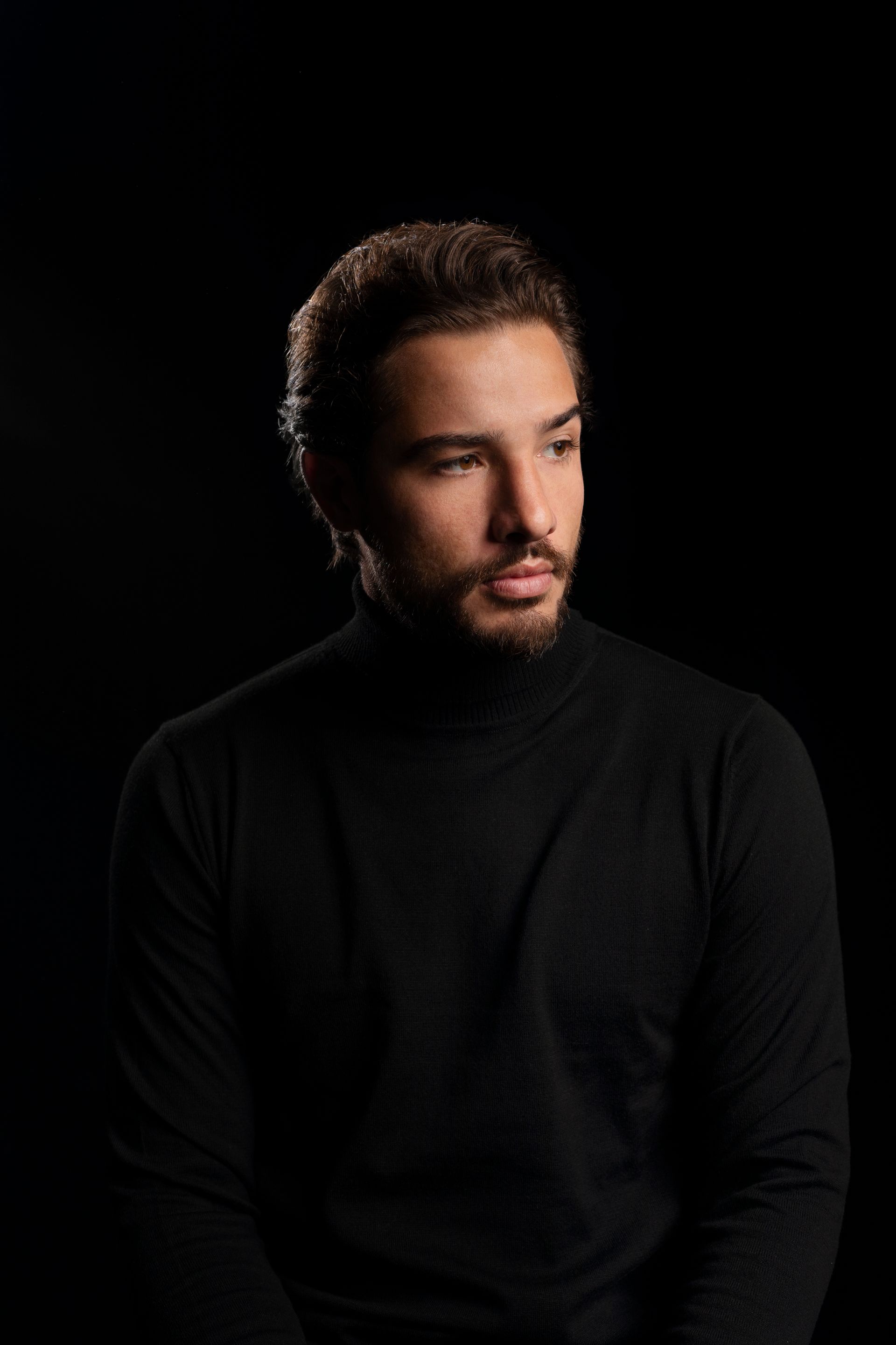 A man with a beard is wearing a black turtleneck sweater.