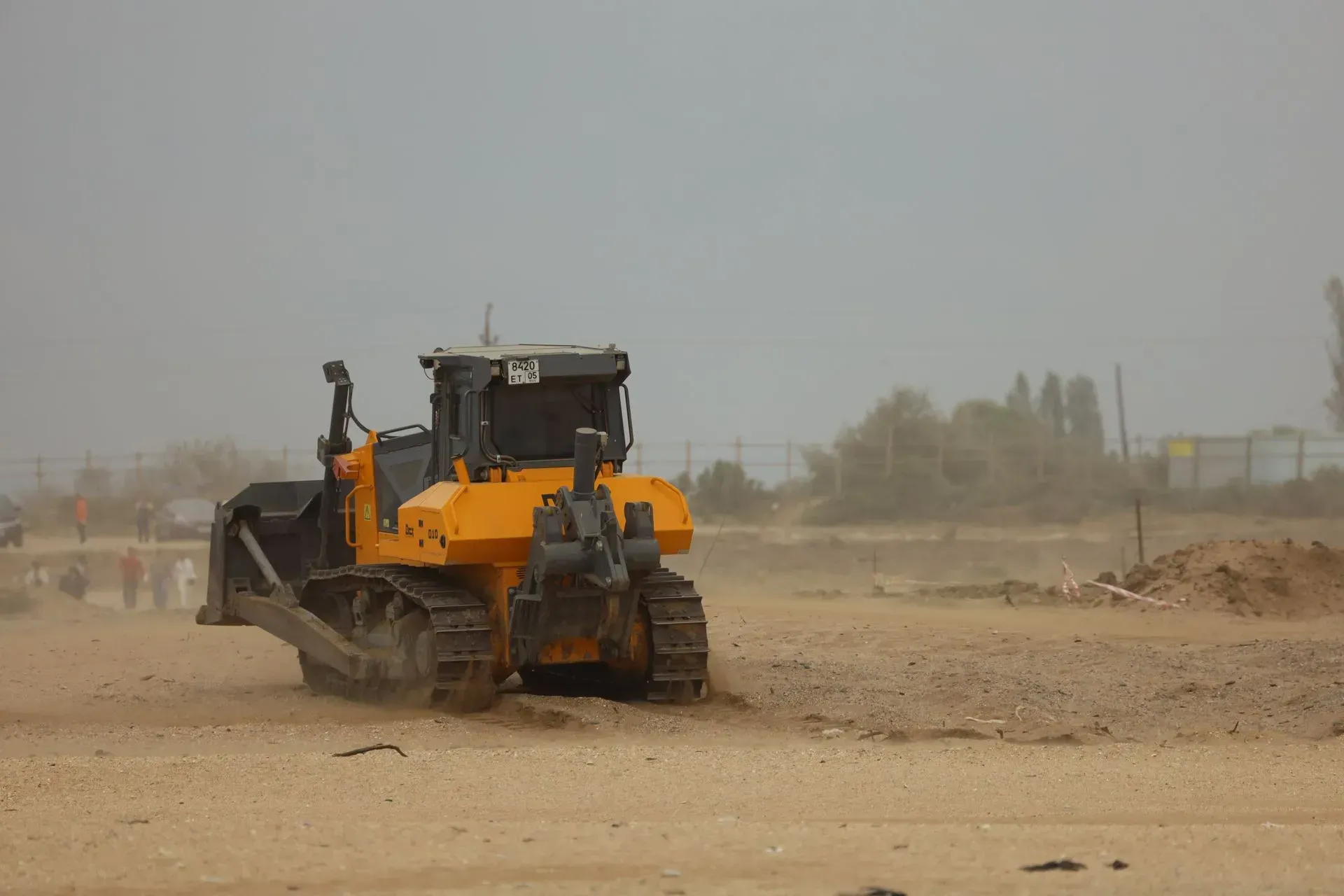 Yellow construction loader kicking up dust on a sandy work site