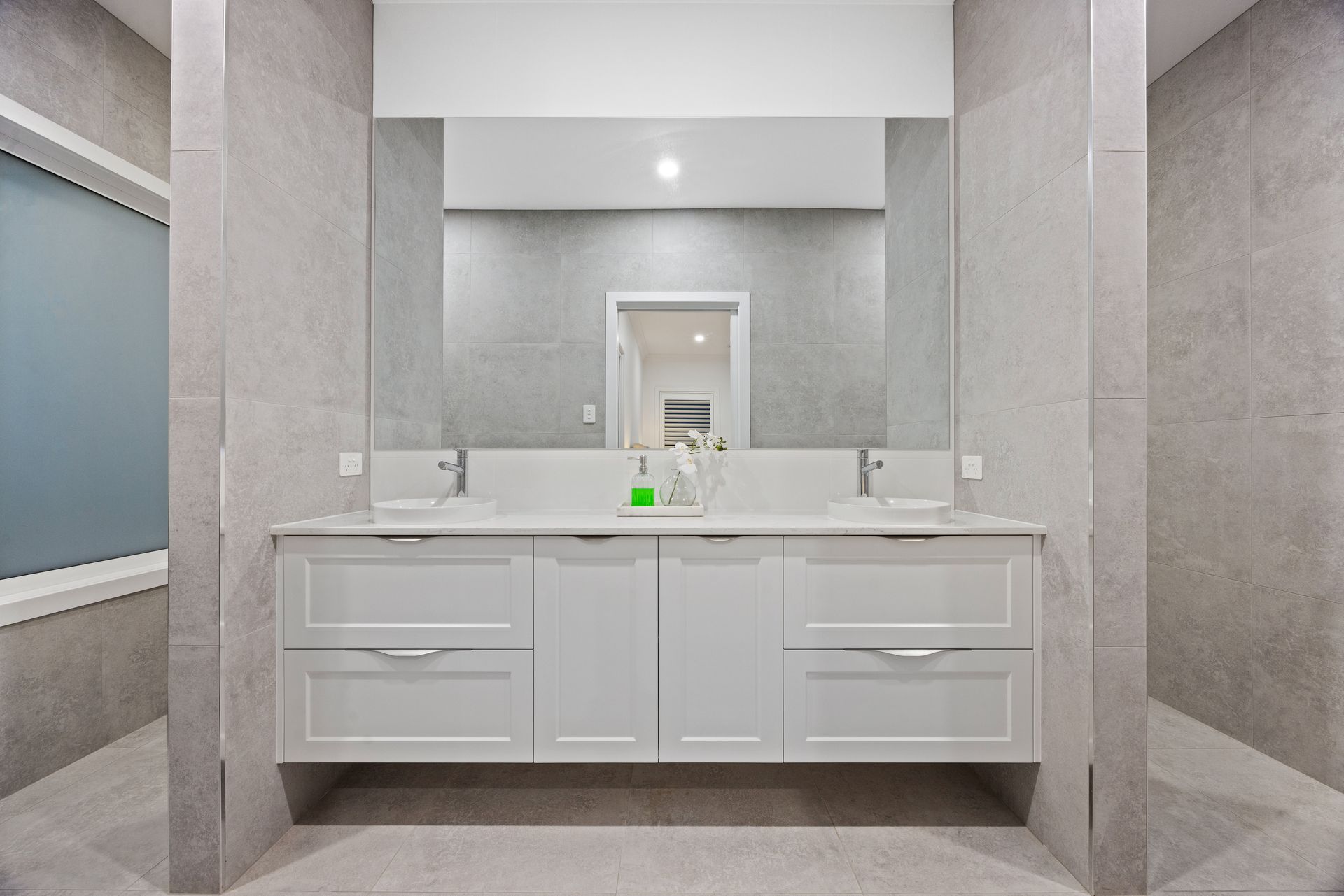 Gray and white bathroom with a double sink vanity, large mirror, and tiled walls.