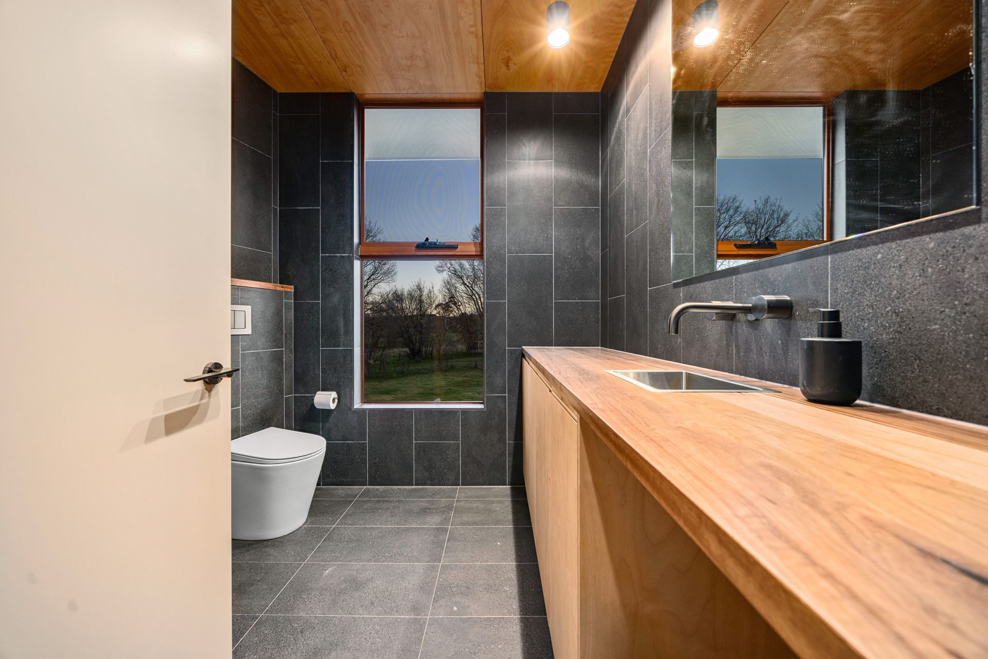Bathroom with gray tile, wooden vanity, window, and modern fixtures.